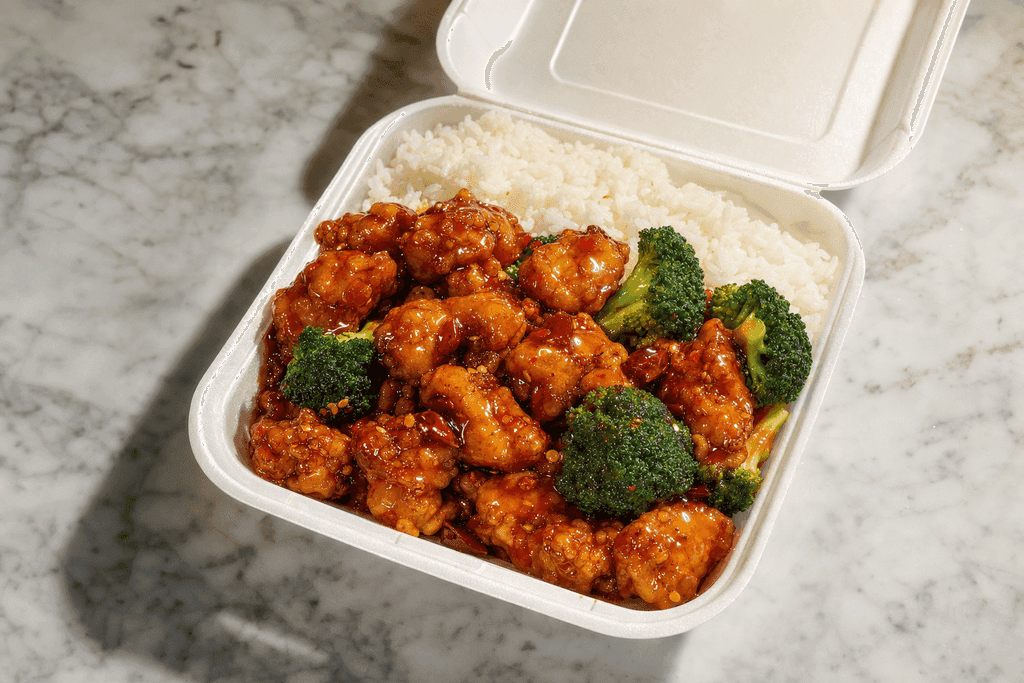 A photorealistic image of a glossy, freshly-served General Tso’s chicken takeout container opened on a clean marble countertop, with golden-brown battered chicken pieces glistening in a vibrant red-orange sauce, surrounded by fluffy white rice and a few bright green broccoli florets, dramatic overhead lighting casting soft shadows, evoking a sense of warmth and indulgence. No characters, text, or humans in the image.
