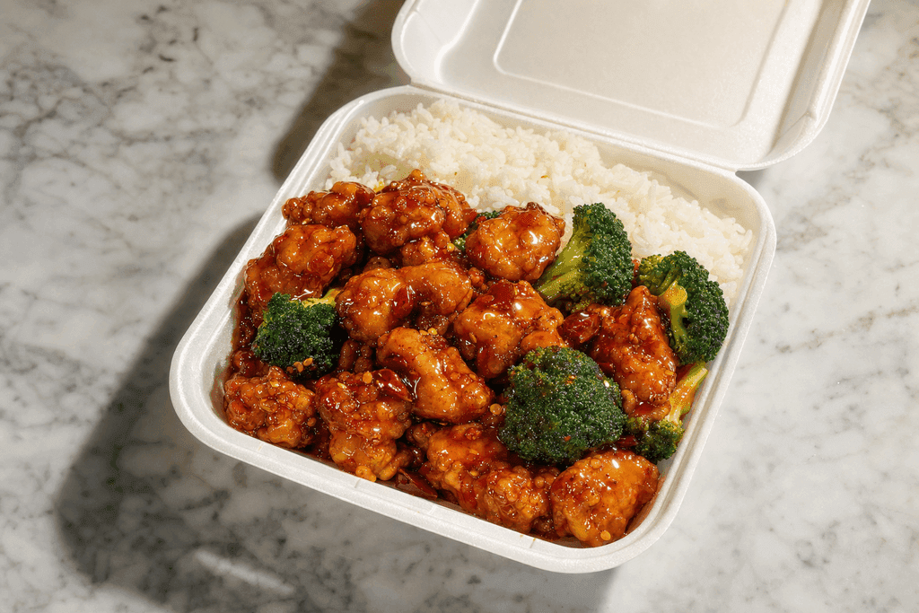 A photorealistic image of a glossy, freshly-served General Tso’s chicken takeout container opened on a clean marble countertop, with golden-brown battered chicken pieces glistening in a vibrant red-orange sauce, surrounded by fluffy white rice and a few bright green broccoli florets, dramatic overhead lighting casting soft shadows, evoking a sense of warmth and indulgence. No characters, text, or humans in the image.