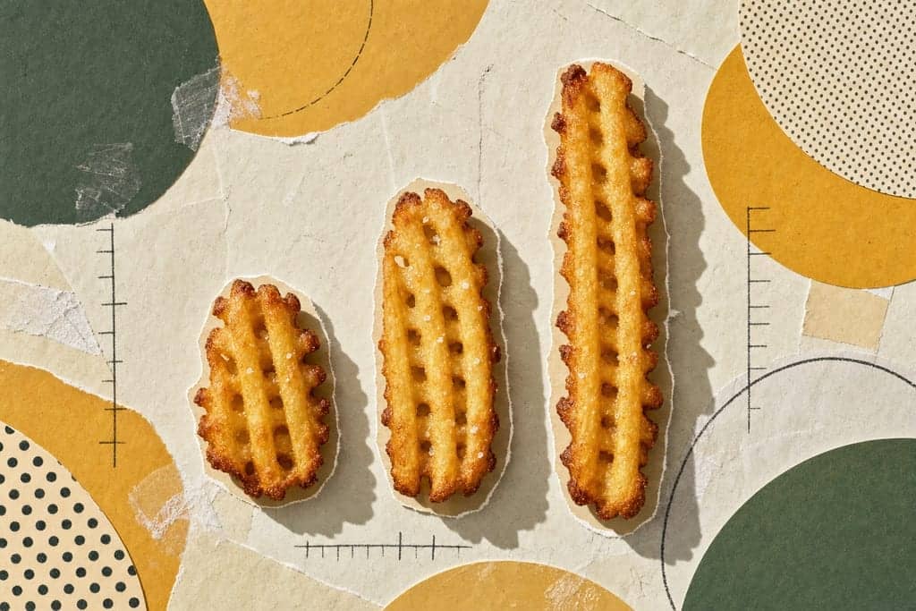 Editorial mixed-media collage of three plain waffle-cut fries as the unmistakable central subject, each fry a different size category implied by scale—one short, one medium, one long—arranged in a crisp vertical lineup across the frame like a minimalist food-comparison study, viewed from a dramatic straight-down overhead angle on a textured torn-paper tabletop; the fries are isolated, evenly spaced, and casting soft cut-out shadows, with crunchy golden ridges, tiny salt crystals, and slightly darker toasted edges emphasized in appetizing detail. Surrounding them are abstract circular and semicircle paper shapes suggesting portion analysis without becoming charts, layered in warm honey, muted mustard, deep sage, and soft cream tones, with halftone scraps and hand-drawn measurement-like tick marks that contain no readable text. The atmosphere is bright, clean, and thoughtfully analytical with a calm morning editorial mood, gentle directional sunlight, subtle glue-stick smears, visible paper grain, rough scissor edges, playful asymmetrical negative space, and absolutely no characters, no humans, and no text anywhere in the image.